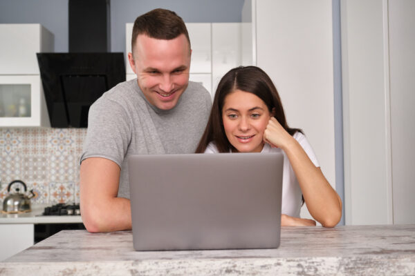 couple standing at kitchen table in front of open laptop computer, reading about lasik